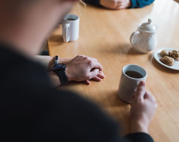 Van Oosterom parents hold hands at the kitchen table, tea and cookies are laid out.